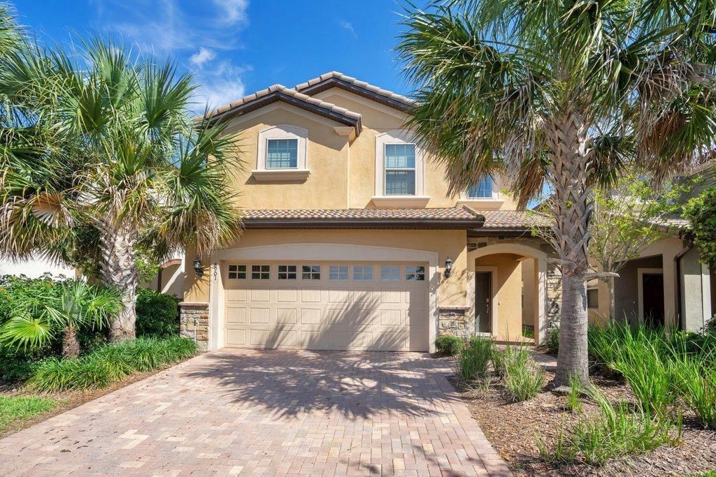 A two-story house with a garage, surrounded by palm trees and a paved driveway.