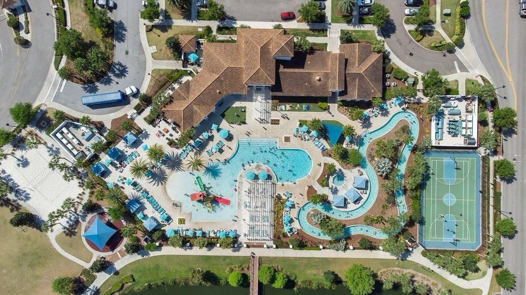 An aerial view of a resort with a large swimming pool, a tennis court, and multiple lounge areas.