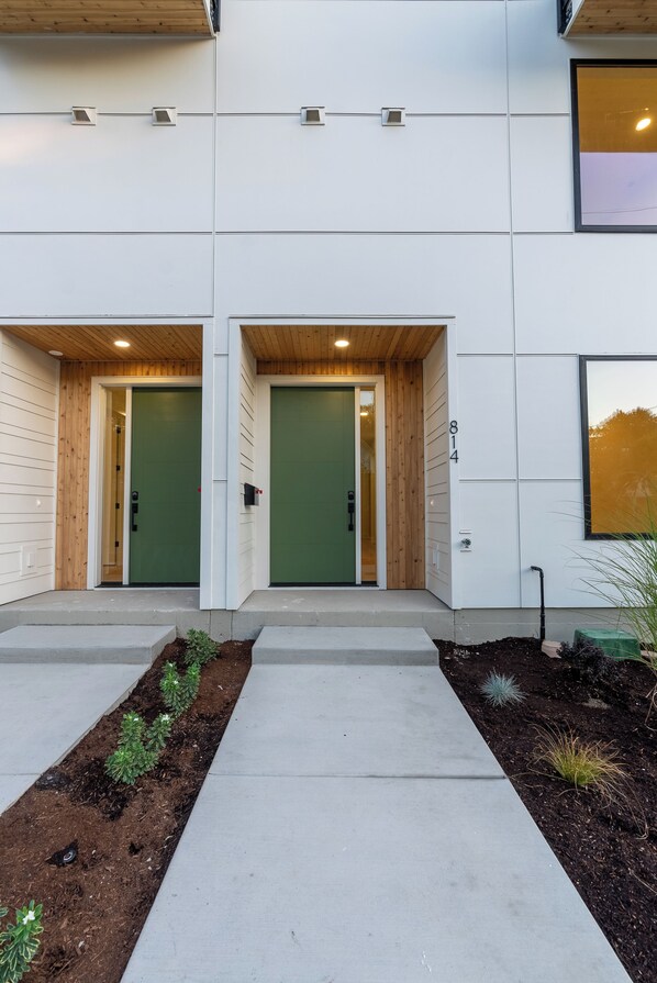 A modern building with two green doors, a concrete pathway, and a small garden area.