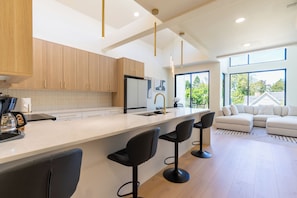 A modern kitchen with a large island, bar stools, and a view of the outdoors through large windows. - Elevated escape, near UO & Hayward (Eugene)