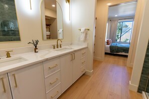 A modern bathroom with a double sink, a mirror, and a vase of flowers.