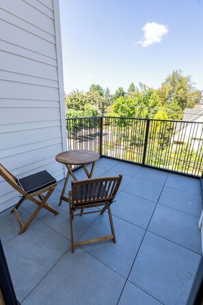 A balcony with two wooden chairs and a small table, a metal railing, and a view of a residential area with trees and houses. - Elevated escape, near UO & Hayward (Eugene)