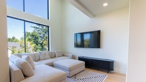 Een moderne woonkamer met een hoekbank, een flatscreen televisie aan de muur en een zwarte salontafel.