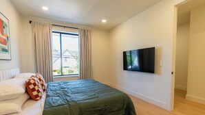 Een slaapkamer met een bed, een televisie aan de muur en een raam met gordijnen.