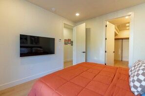 Quarto com cama, televisão na parede e porta que dá para outro espaço.