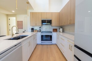 A modern kitchen with white cabinetry, stainless steel appliances, and a wooden floor. - Elevated escape, near UO & Hayward (Eugene)
