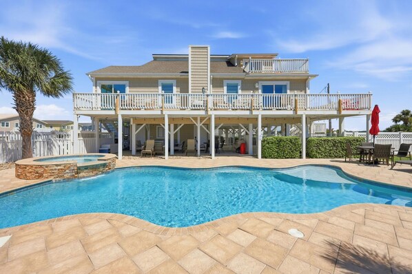 Una casa de dos pisos con piscina, un patio cubierto y un deck cercado.