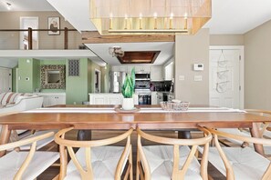 A spacious dining area with a wooden table and chairs, a hanging light fixture, and a view of the kitchen and living area. - Palm Cove | Luxury Channel Home + Coastal Escape (North Myrtle Beach)