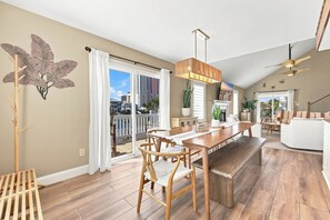 A spacious living area with a wooden dining table, chairs, and a balcony with a view of the city. - Palm Cove | Luxury Channel Home + Coastal Escape (North Myrtle Beach)