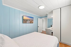 A bedroom with a bed, a painting, a wardrobe, and a door leading to another room. - Elvi's Beach House | Spacious 6BR Duplex (North Myrtle Beach)
