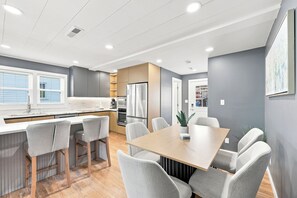 A modern kitchen with a dining area, wooden flooring, and a view of the outdoors. - Elvi's Beach House | Spacious 6BR Duplex (North Myrtle Beach)