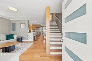 A modern interior with a staircase leading to a second floor, a kitchen area, and a seating area with a sofa and a coffee table. - Elvi's Beach House | Spacious 6BR Duplex (North Myrtle Beach)