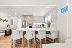 A modern kitchen with a central island, stainless steel appliances, and a seating area with cushioned chairs. - Elvi's Beach House | Spacious 6BR Duplex (North Myrtle Beach)