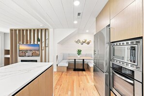 A modern kitchen with a built-in oven, a dining area with a white table and bench, and a TV mounted on the wall. - Elvi's Beach House | Spacious 6BR Duplex (North Myrtle Beach)
