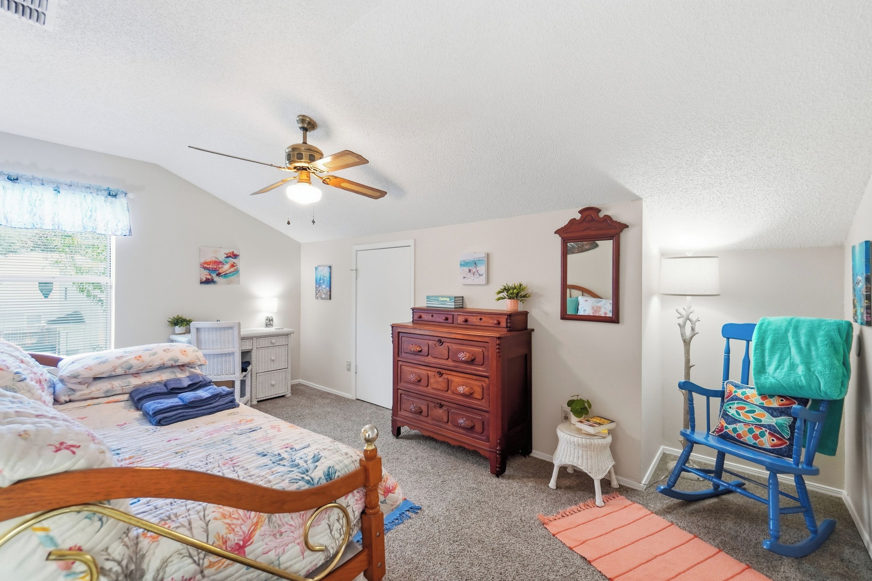A bedroom with a bed, dresser, chair, and a ceiling fan.
