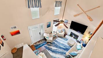 A spacious living room with a large TV, a fireplace, and a ceiling fan.