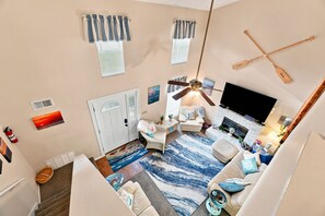 Ein geräumiges Wohnzimmer mit großem Fernseher, Kamin und Deckenventilator.