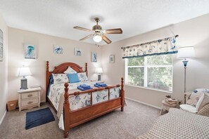 A bedroom with a wooden bed, two bedside tables with lamps, a ceiling fan, a window with blinds, and artwork on the walls. - Serene Retreat w/ Private Backyard (Jacksonville)