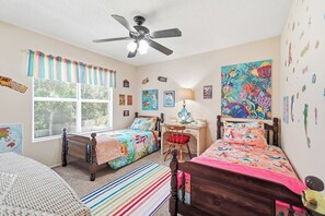 A bedroom with two beds, a desk, a chair, a ceiling fan, and a window with blinds. - Family 4BR Home | Fenced Yard | 5 Min to Beach (Jacksonville)