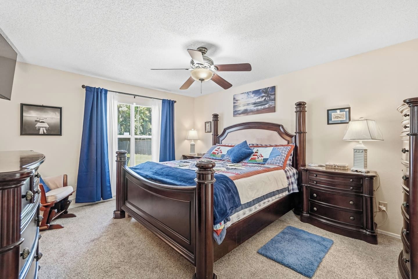 A bedroom with a bed, a ceiling fan, a dresser, a nightstand, and a window with curtains.