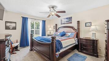 A bedroom with a bed, a ceiling fan, a dresser, a nightstand, and a window with curtains.