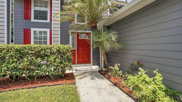 A residential building with a red door, a pathway leading to the entrance, and a variety of plants and shrubs.