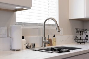 A modern kitchen with a stainless steel sink, a dish rack, and a window with blinds. - Cozy Casa | Contemporary 2BR Home · La Mesa (La Mesa)