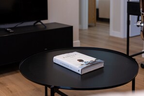 A book titled 'The Kinfolk Table' on a small round table in a room with a black TV stand and a wooden floor. - Cozy Casa | Contemporary 2BR Home · La Mesa (La Mesa)