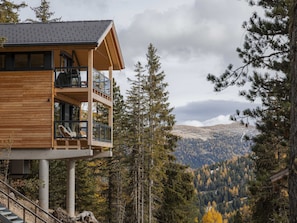A wooden cabin with a balcony overlooking a forested valley. - 03_NTH029_Premium Chalet mit Sauna und Hot Tub by Interhome (Turrach)
