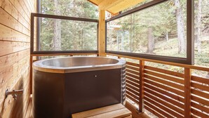 Una baita di legno con vasca idromassaggio e ampie finestre che si affacciano su una foresta.