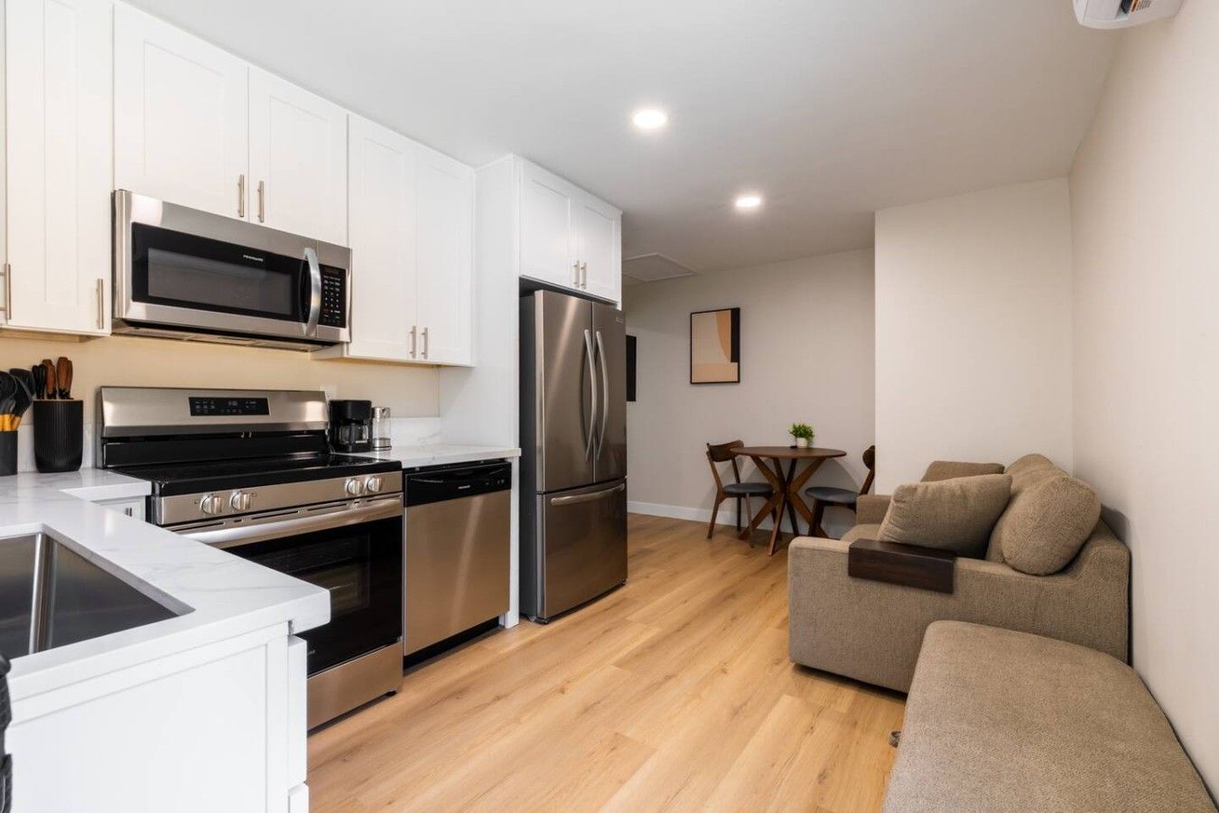 A modern kitchen with stainless steel appliances, a dining area with a table and chairs, and a beige sofa.
