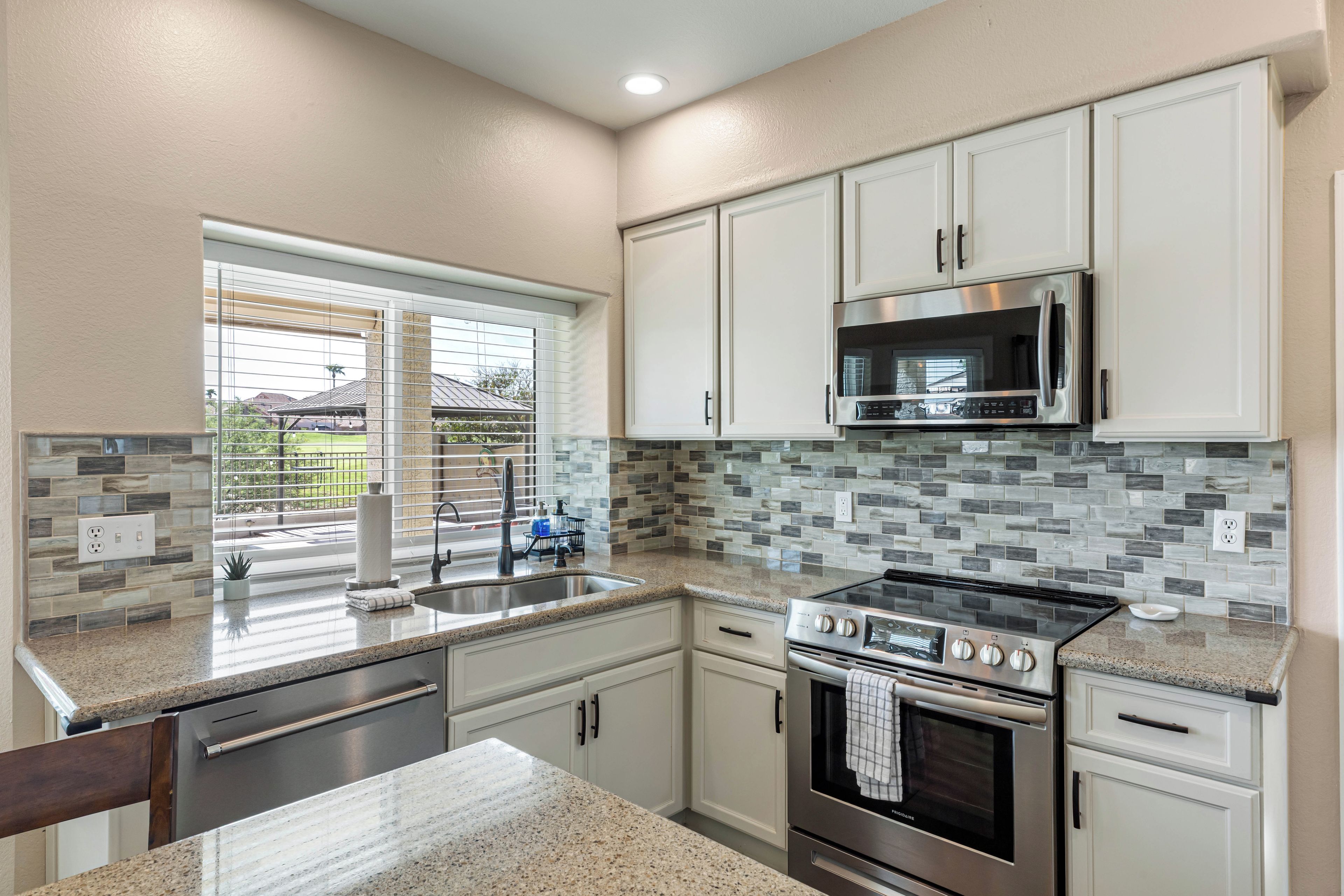 A kitchen with white cabinets, a stainless steel microwave, a gas stove, and a tiled backsplash.