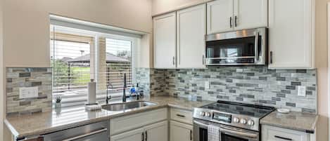 A kitchen with white cabinets, a stainless steel microwave, a gas stove, and a tiled backsplash.