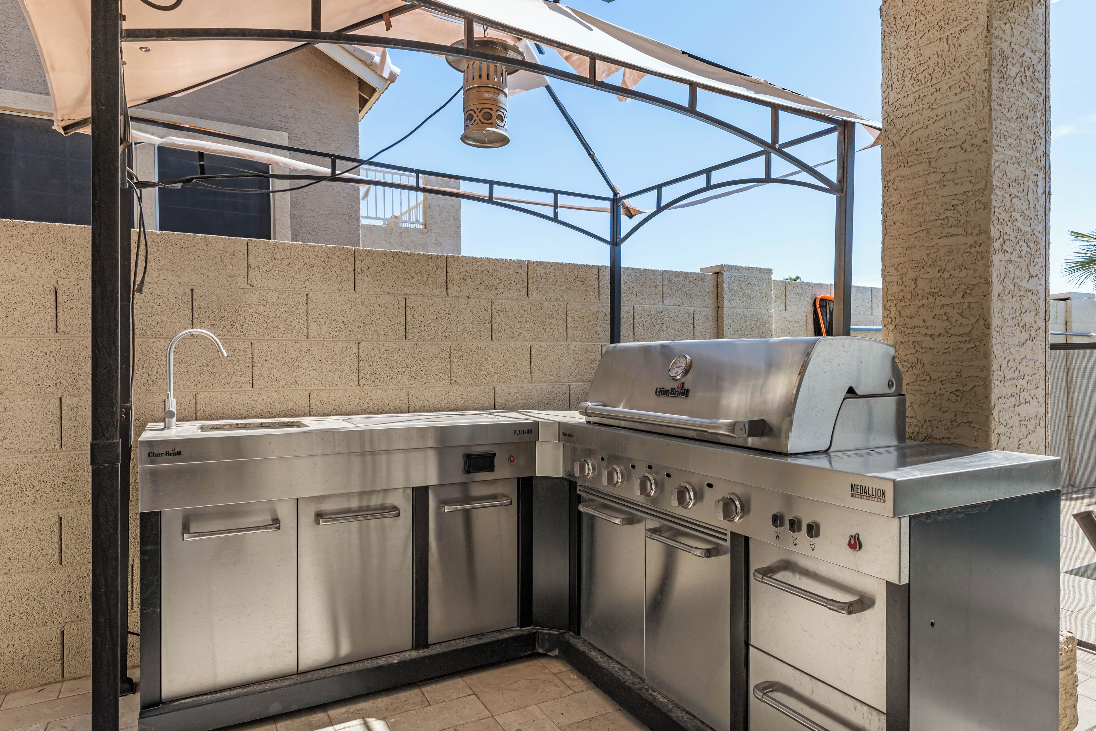 A stainless steel outdoor kitchen with a built-in grill, a sink, and a ventilation hood.