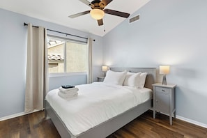 Ein Schlafzimmer mit einem Bett, Nachttischen, einem Deckenventilator und einem Fenster mit Vorhängen.