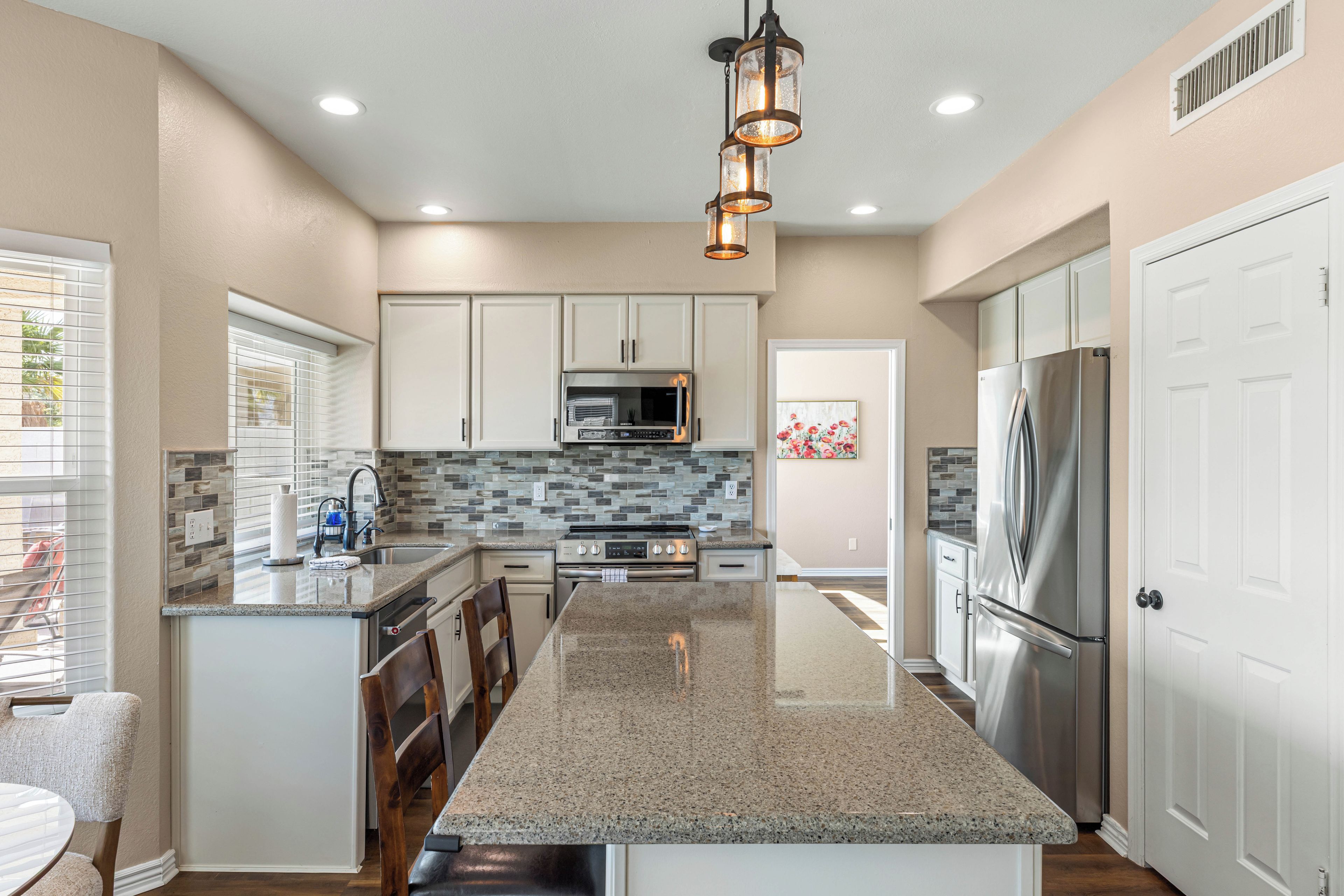A modern kitchen with a central island, stainless steel appliances, and a tiled backsplash.