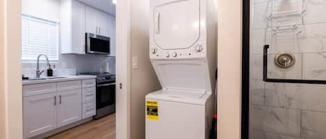A laundry room with a washing machine, a microwave, and a shower area.