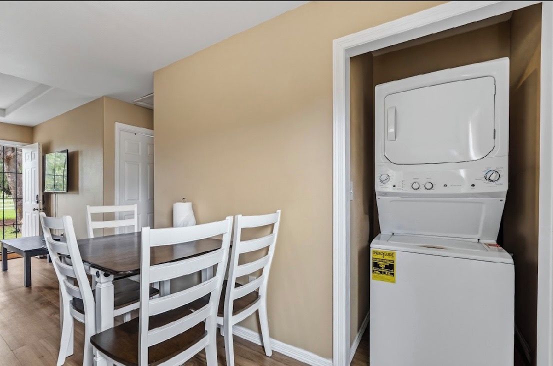 Une pièce comprenant une table à manger et des chaises, un lave-linge blanc, et une porte donnant sur une autre pièce.