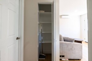 Ein Zimmer mit geschlossener Tür, einem Schrank mit Regalen, einem Besen und einem Sofa mit Kissen.