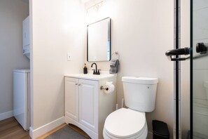 A bathroom with a white toilet, a sink with a mirror above it, and a shower area. - Cozy Casa | Sunny Santee Sanctuary (Santee)