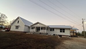 A two-story white house with a porch and a covered area, surrounded by a gravel driveway and a grassy area. - Cozy 2-bedroom house in Bowdon (Bowdon)