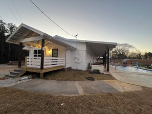 Uma casa térrea com varanda coberta, um pequeno jardim frontal e uma piscina.