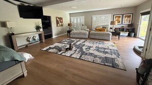 A spacious living room with a large rug, a sofa, a chair, and a television mounted on the wall. - Cozy 2-bedroom house in Bowdon (Bowdon)