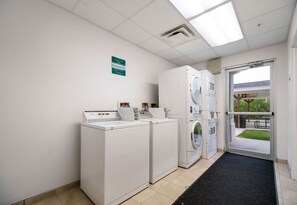 A laundry room with stacked washers and dryers, a sign indicating a smoking area, and a door leading outside. - Budget-Friendly Ingleside Room l Kitchen + Pool Access | Free Parking (Ingleside)