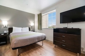 Un dormitorio con cama, lámparas de noche, cómoda, televisor y ventana con cortinas.