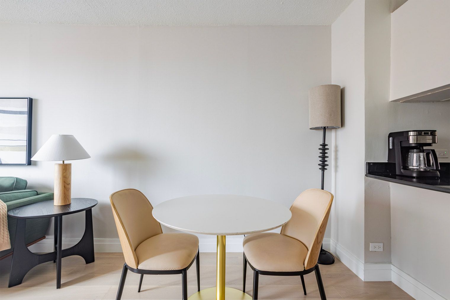 Uma área de refeições moderna com uma mesa redonda, duas cadeiras, um abajur e uma máquina de café.