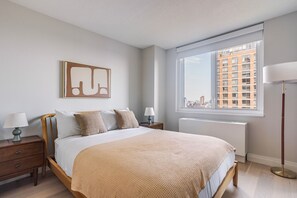 Ein modernes Schlafzimmer mit einem großen Bett, Nachttischlampen, einer Heizung und Blick auf die Stadt durch ein Fenster.