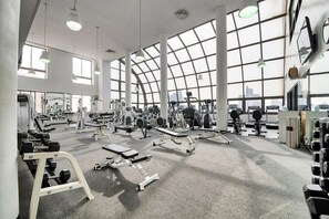 Ein Fitnessstudio mit unterschiedlichen Trainingsgeräten, großen Fenstern und hoher Decke.