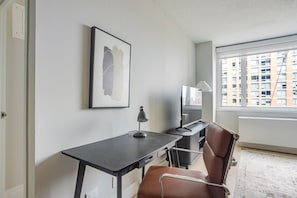 Ein modernes Zimmer mit Schreibtisch, Stuhl, Fernseher und einem gerahmten Kunstwerk an der Wand.