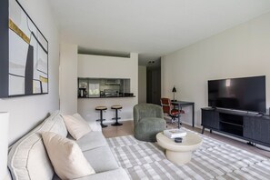 Un soggiorno moderno con un divano, un tavolino, una TV e un angolo cottura sullo sfondo.